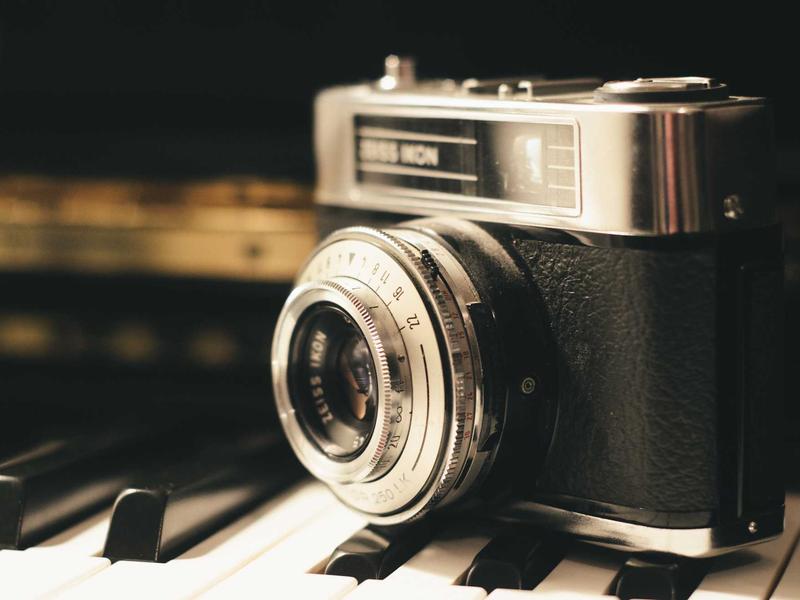 Vintage film camera resting on piano keys in warm low light, evoking quiet pre-dawn work.