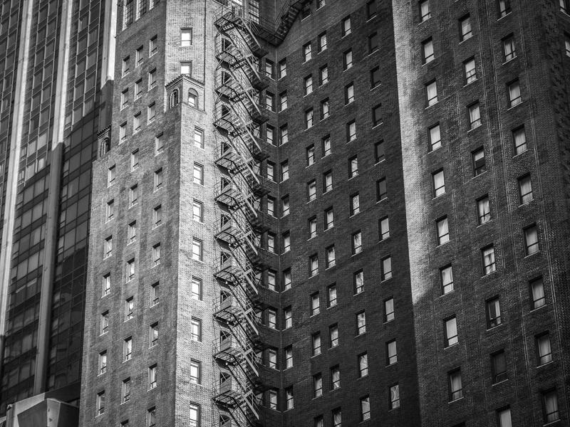 Tall brick city building with a zigzag exterior fire escape and repeating windows, shown in black-and-white.