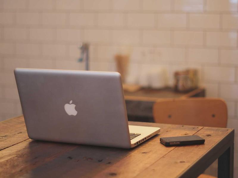 Unattended laptop and phone on a wooden table in the bakery's casual workspace, suggesting remote work.