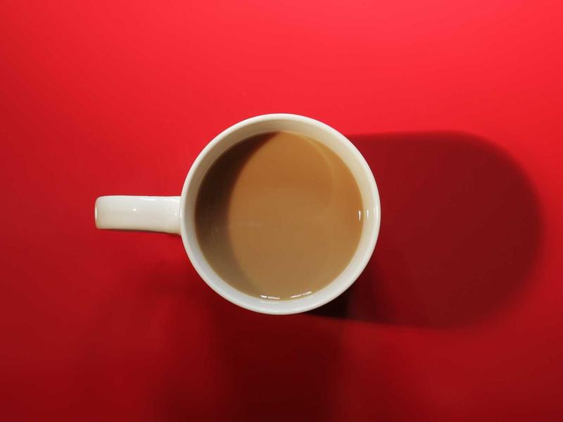 White mug of coffee with milk on a bright red surface, casting a long shadow to the right.