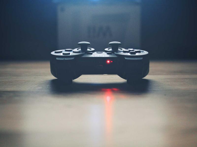 Black game controller on a wooden table with a red LED and reflected glow in low moody lighting.